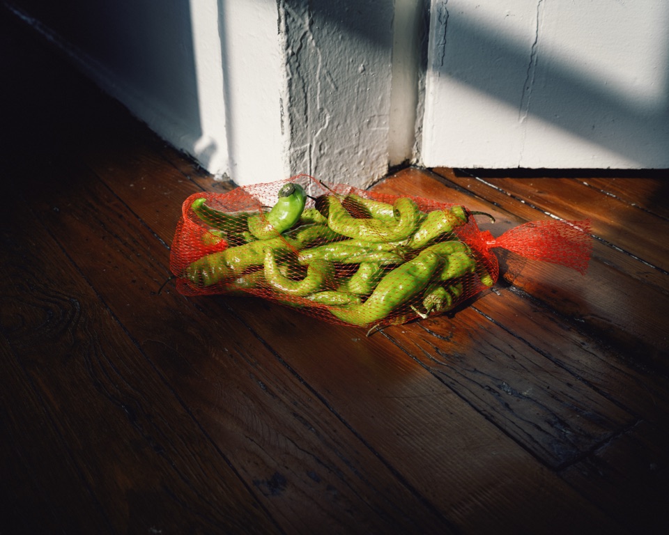 Green peppers in a red mesh bag on a wooden floor