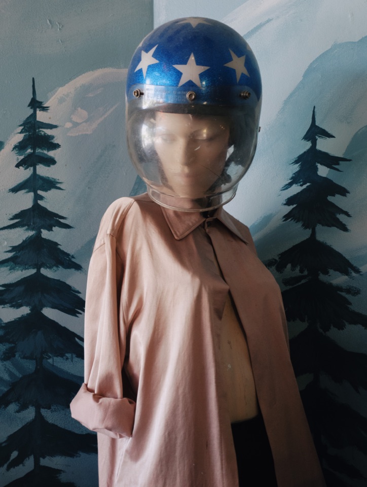 A mannequin in a helmet in front of painted pine trees